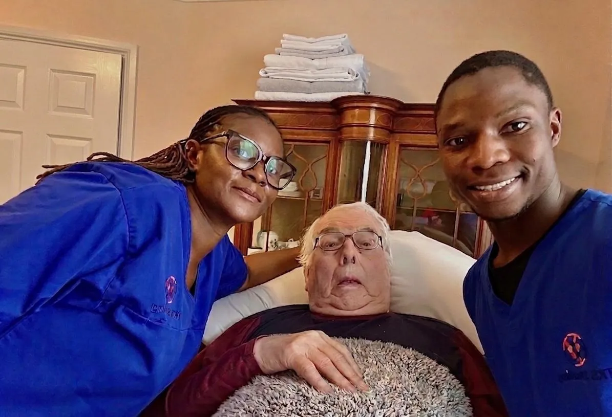 Two TKS Staffing carers in blue uniforms with a gentleman they support at his home